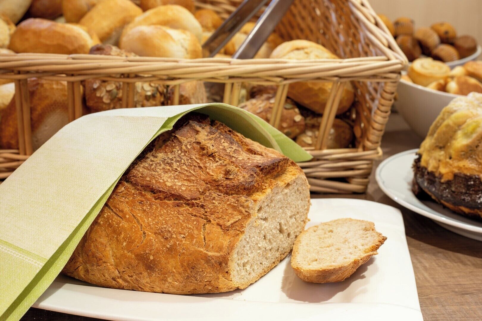 A loaf of bread on a plate with a basket of various breads in the background.