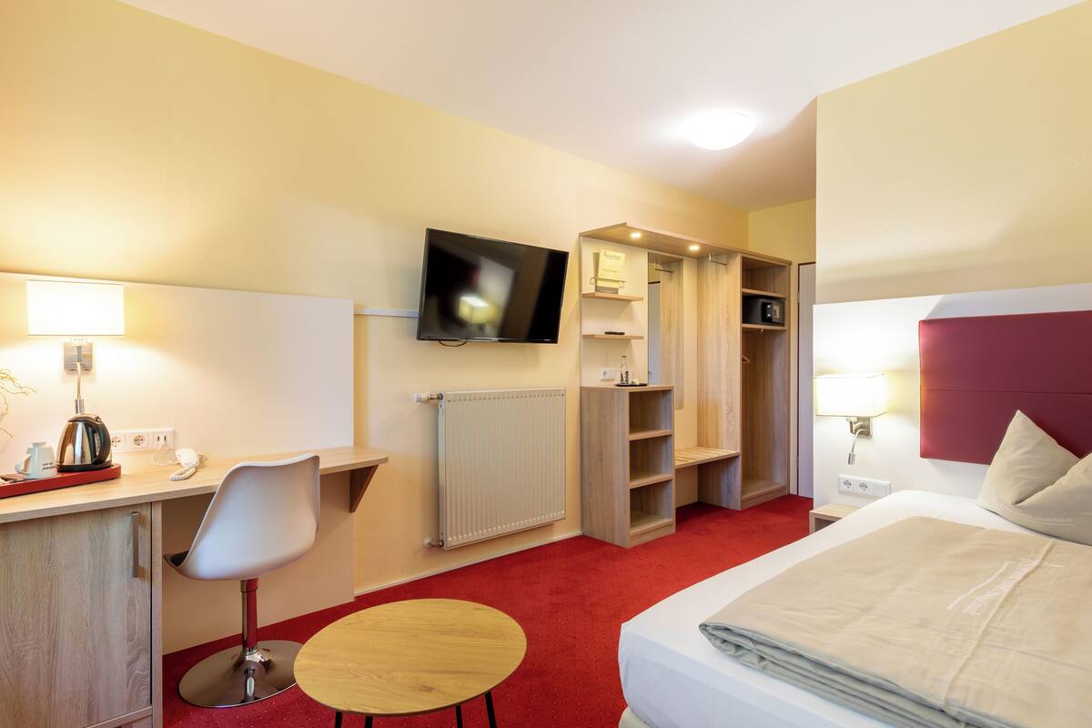 Habitació d'hotel amb llit, escriptori amb cadira, televisió, armari i una taula petita.