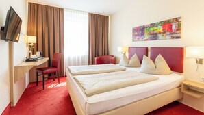 Habitación de hotel con cama, escritorio, silla, televisor y un cuadro en la pared.