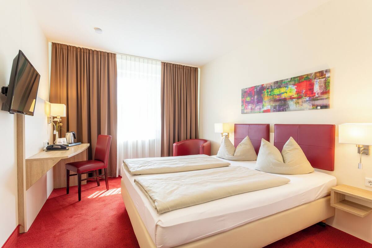 Una habitació d'hotel amb un llit, escriptori, cadira, televisió i un quadre a la paret.