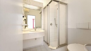 Un baño moderno con cabina de ducha de vidrio, un lavamanos blanco y un inodoro.