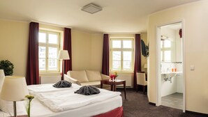 Habitación de hotel con cama, sofá, escritorio y baño visible a través de una puerta abierta.