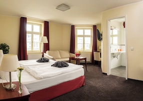 Habitación de hotel con cama, sofá, escritorio y baño visible a través de una puerta abierta.