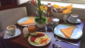 Una mesa de desayuno con platos de comida, una taza de café, un vaso de jugo, una botella de jugo de manzana, una cesta de pan y un jarrón con flores.