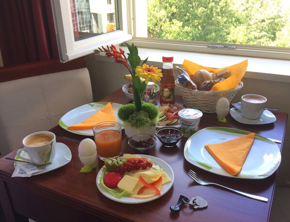 A breakfast table with plates of food, a coffee cup, a juice glass, a bottle of apple juice, a basket of bread, and a vase with flowers. - AppartementHotel SchlafGut Leipzig (Leipzig)