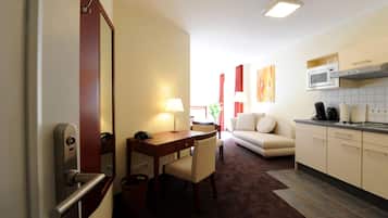 A hotel room with a dining area, a sofa, a kitchen with a microwave, and a large mirror.