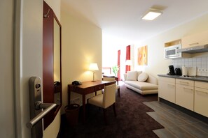 Une chambre d’hôtel comprenant un coin repas, un canapé, une cuisine équipée d’un four à micro-ondes et un grand miroir.