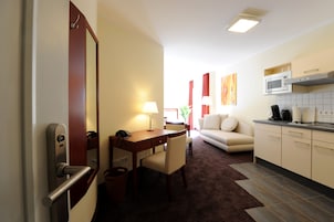 Habitación de hotel con zona de comedor, sofá, cocina con microondas y un espejo grande.