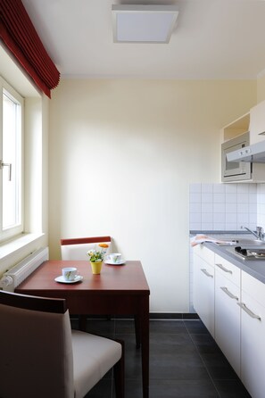 A compact kitchen with a dining table, chairs, a microwave, and a sink. - AppartementHotel SchlafGut Leipzig (Leipzig)