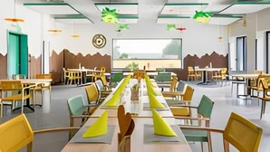 Ein geräumiger Essbereich mit langen Tischen und Stühlen, grünen Hängeleuchten und Blick ins Freie.