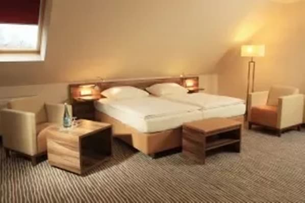 Quarto de hotel com uma cama grande, duas mesas de cabeceira, um criado-mudo, uma cadeira e um abajur.