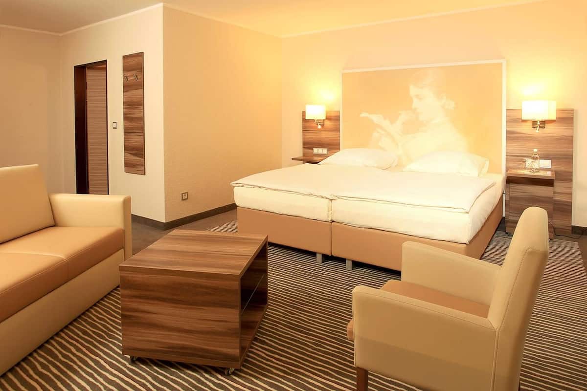 A hotel room with a bed, two bedside tables, a wooden coffee table, a sofa, and a patterned carpet.