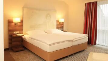 Una habitación de hotel con una cama grande, dos mesitas de noche, una lámpara de pared y una ventana con cortinas.