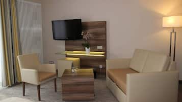 Ein modernes Hotelzimmer mit einer Couch, einem Sessel und einem Flachbildfernseher, der an einem Holz-Kopfteil befestigt ist.