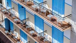A multi-story building with balconies, each with outdoor seating and a white umbrella. - Hostal Ferrer (Sant Antoni de Portmany)