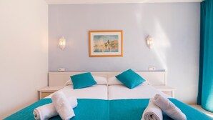 A double bed with teal bedding and pillows, a framed painting on the wall, and two wall-mounted light fixtures. - Hostal Ferrer (Sant Antoni de Portmany)