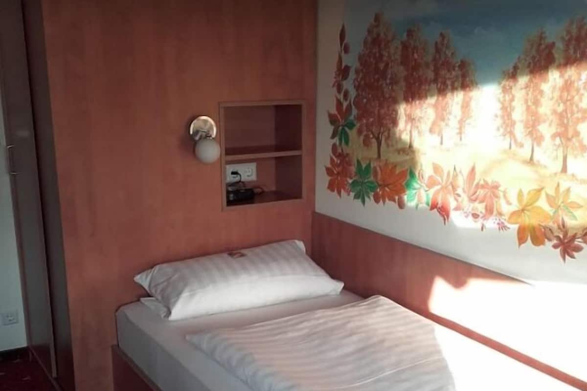 Una cama individual con ropa de cama blanca, una repisa en la pared y un mural de hojas otoñales.