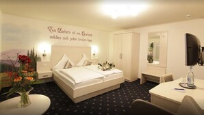 A hotel room with a bed, a desk, a chair, a mirror, and a wall with a decorative phrase.