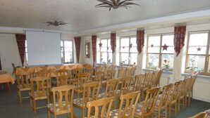 A conference room with rows of wooden chairs and tables, large windows with curtains, and a whiteboard.