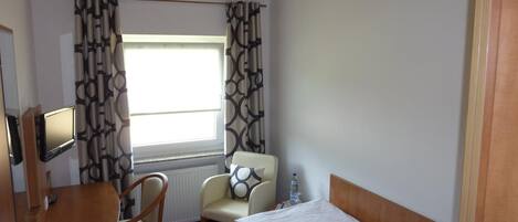A hotel room with a bed, a desk with a chair, a television, and a window with curtains.