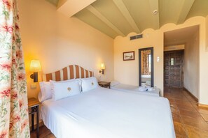 Un dormitorio con una cama grande, dos mesitas de noche, una lámpara de pared, un cuadro enmarcado y una puerta que da a otra habitación.
