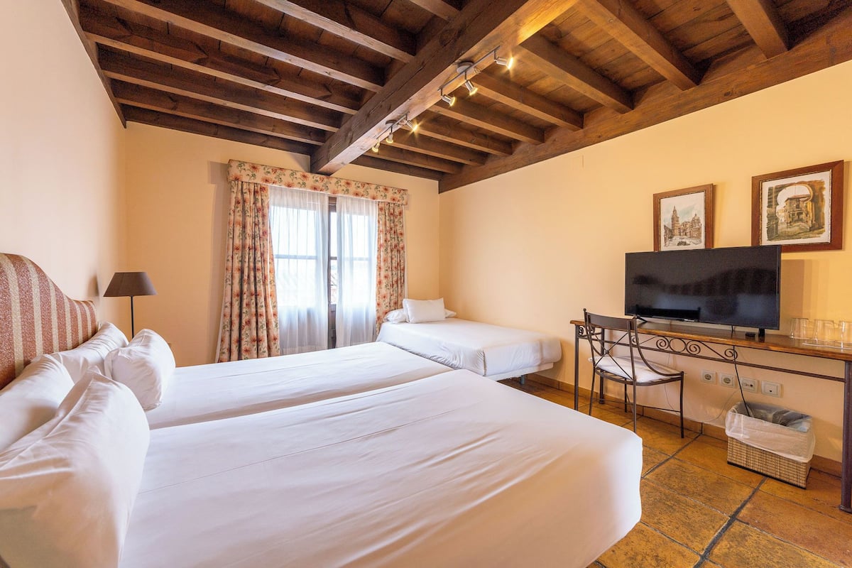 A hotel room with two beds, a desk with a television, and a chair.