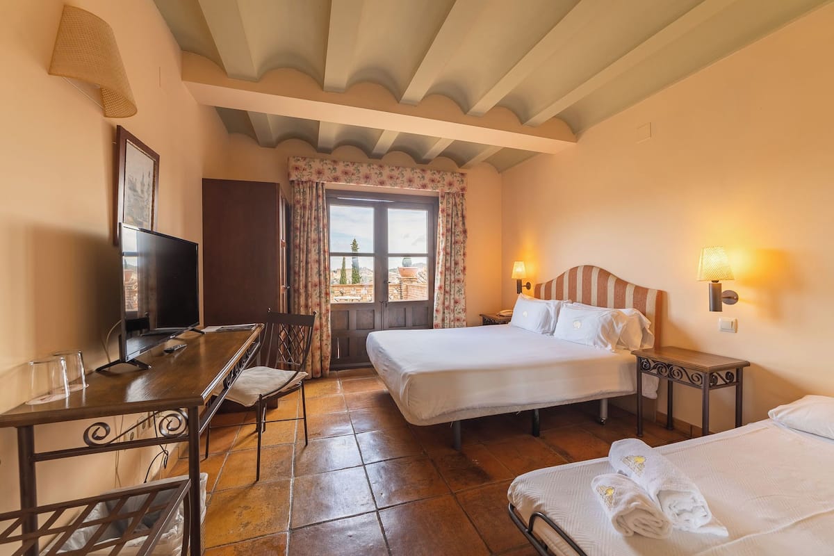 A hotel room with two beds, a desk with a chair, a TV, and a window with curtains.