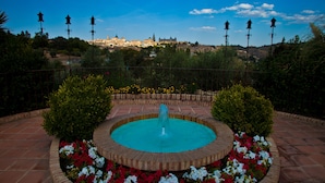Una fuente rodeada de flores y una vista de un edificio histórico al fondo.