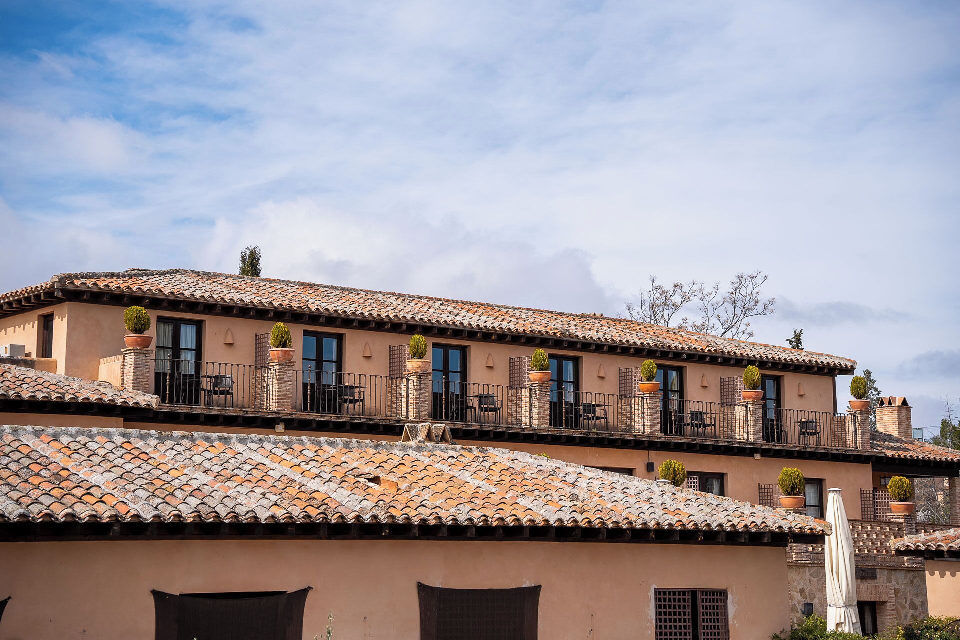 A multi-story building with terracotta tiled roofs, balconies with black railings, and potted plants.