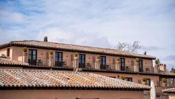 A multi-story building with terracotta tiled roofs, balconies with black railings, and potted plants.