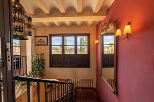 Una escalera con vistas a un paisaje urbano a través de una ventana, un espejo con un marco decorativo y una lámpara fijada a la pared.