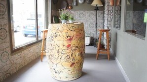 A room with a large, artistically decorated barrel, a small stool, and a potted plant on a table. - Hotel MR (Tarragona)