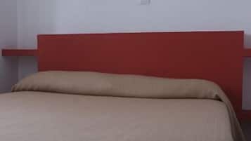 Una cama con cabecera roja y colcha color beige en una habitación con un cuadro abstracto y colorido en la pared.