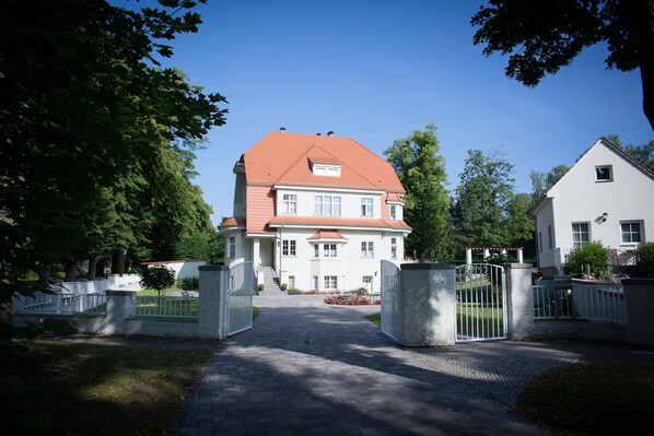 A large, white house with a red roof, a paved driveway, and a gated entrance. - Villa Ingeborg (Fürstenberg-Havel)