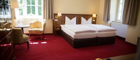 A hotel room with a large bed, a chair, a table with fruit, and a window with curtains.