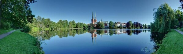A serene lakeside view with a church, a pathway, and lush greenery. - Am Mühlenteich (Lübeck)