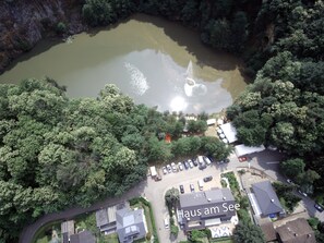 An aerial view of a lakeside property with a swimming area, a parking lot, and several buildings. - Hotel Haus am See (Sinzheim)