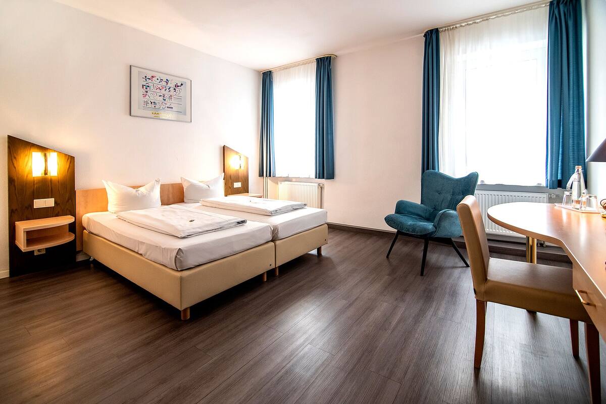 Een hotelkamer met een tweepersoonsbed, een bureau, een stoel en een raam met gordijnen.