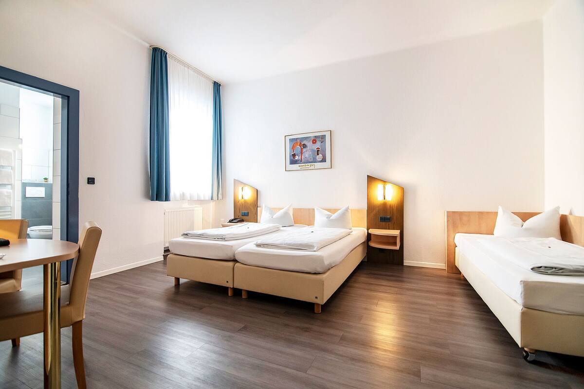 Een hotelkamer met een tweepersoonsbed, een eenpersoonsbed, een bureau en een stoel.