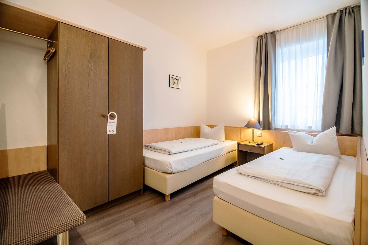 Een hotelkamer met twee bedden, een kledingkast, een bureau en een raam met gordijnen.