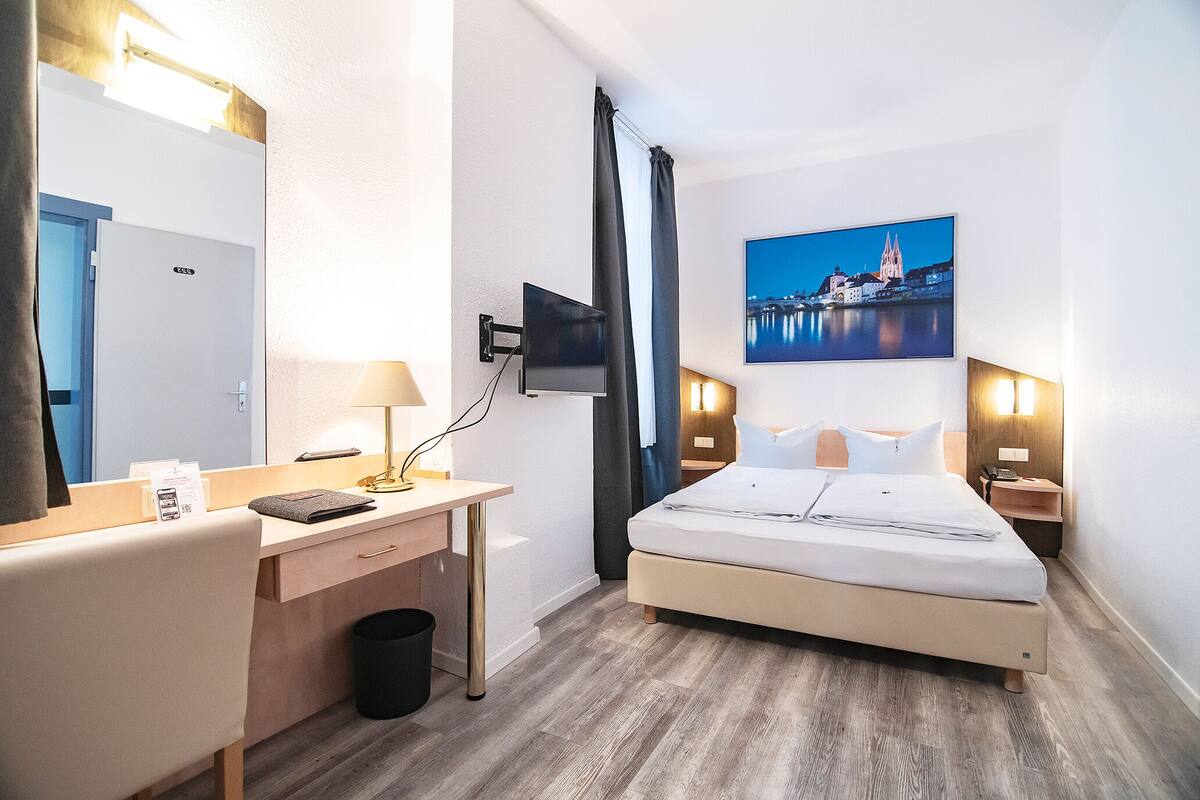 Een hotelkamer met een bed, bureau, stoel en een aan de muur bevestigde televisie.