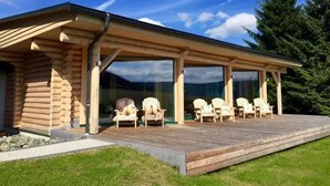 A log cabin with a covered outdoor deck and several Adirondack chairs.