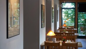 Un restaurante con mesas y sillas de madera, cuadros en las paredes y vistas a zonas verdes al exterior.