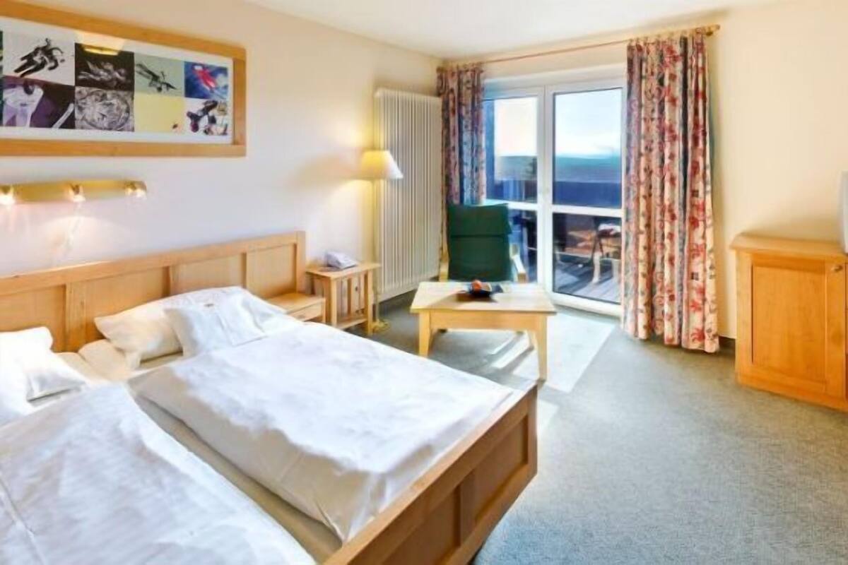 Ein Hotelzimmer mit Bett, Schreibtisch, Stuhl, Fernseher und Meerblick durch ein großes Fenster.
