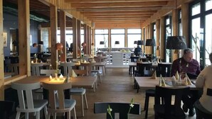 A spacious restaurant with wooden beams, large windows, and a central counter.