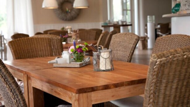 A wooden dining table with wicker chairs, a vase with flowers, and a salt and pepper shaker. - Golfhotel Gut Winterbrock (Rheine)