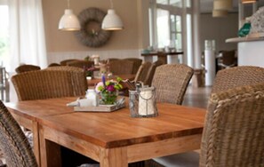 Una mesa de comedor de madera con sillas de mimbre, un florero con flores y un salero y pimentero.