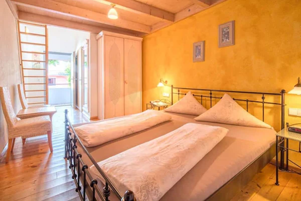 A room with two beds, a chair, and a small table with a lamp.