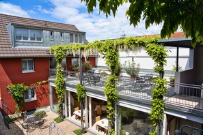 A courtyard with outdoor seating, a red building, and a covered area with a roof.