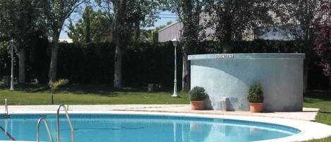 A swimming pool with a clear blue water surface, surrounded by a well-maintained lawn and trees.